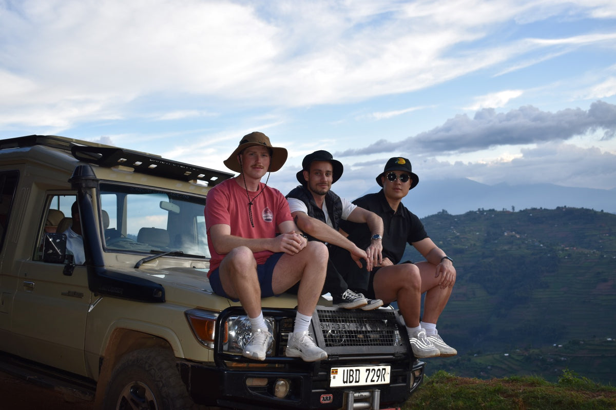 Three people sitting on a vehicle with a scenic background in Uganda