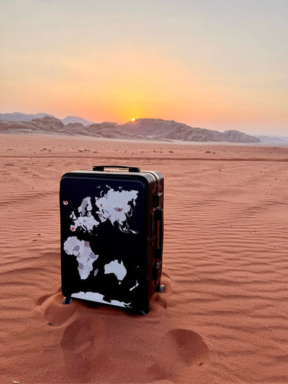 Black suitcase with a world map design in the desert at sunset