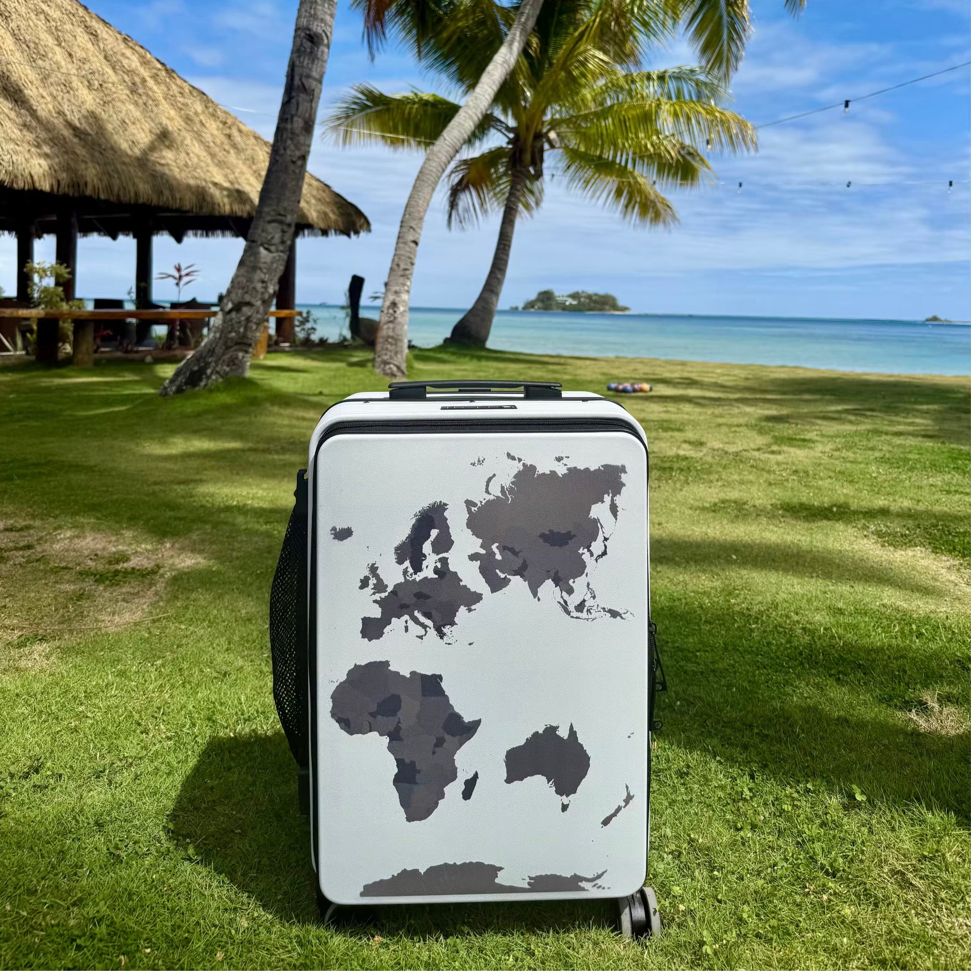 Suitcase with world map design on grass near a tropical beach