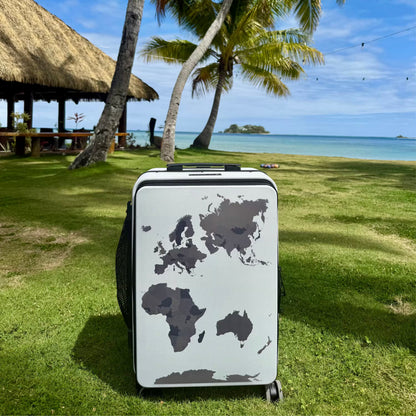 Suitcase with world map design on grass near a tropical beach
