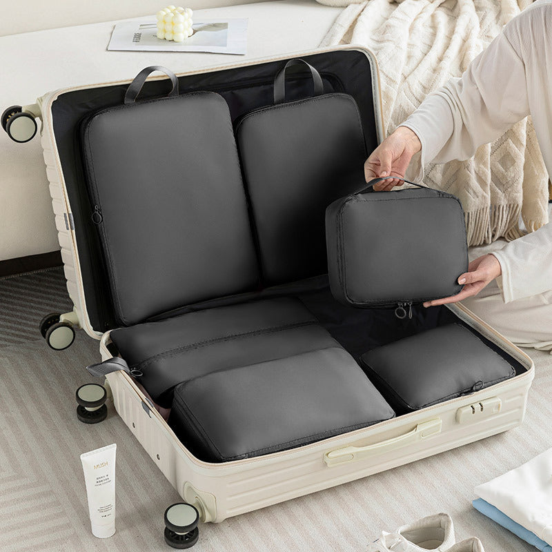 Person packing gray travel bags into an open suitcase on a bed.