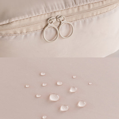 Close-up of a beige fabric with water droplets and a zipper, on a light pink background.