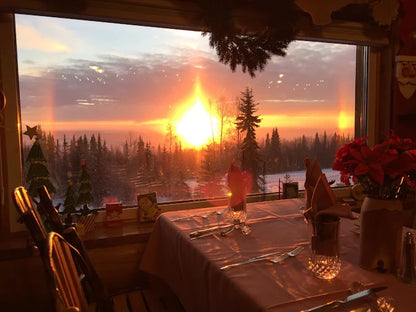 Dining room with a large window showing a sunset over a forest, decorated for Christmas.