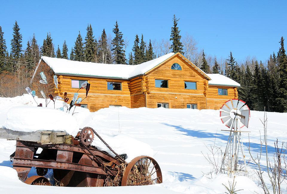 Wooden cabin in a snowy landscape with a windmill and old tractor.