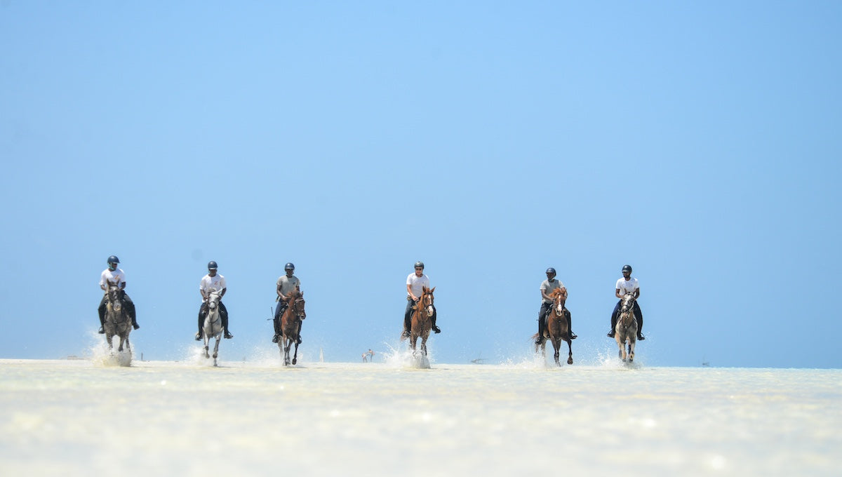 People riding horses on a flat, white landscape under a clear blue sky in zanzibar.